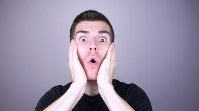 A very shocked man grabs his cheeks with his hands