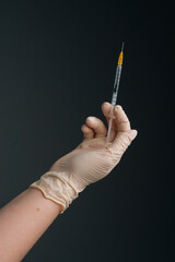 Vertical studio shot of healthcare worker with protective gloves is holding syringe, closeup. Close-up of unrecognizable nurse wearing white latex gloves holding syringe on isolated black background.