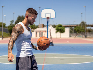 Hombre joven con tatuajes entrenando baloncesto en la calle