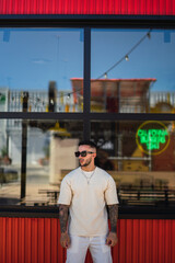 Chico joven atractivo tatuado posando frente a ventana de restaurante