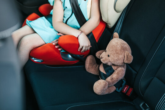 Little girl sitting in a car on a safety child car seat with her teddy bear.