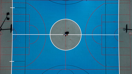 Toma de drone en cancha de baloncesto con un chico en medio de ella  - obrazy, fototapety, plakaty