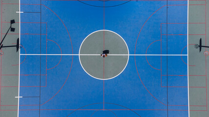 Toma de drone en cancha de baloncesto con un chico en medio de ella 