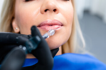 Attractive young woman is getting a rejuvenating injections. She is sitting calmly at clinic. The expert beautician is filling female lips by hyaluronic acid.