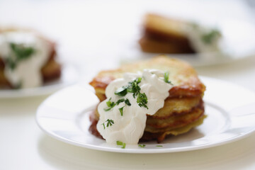 Potato pancakes with sour cream and herbs on plate closeup