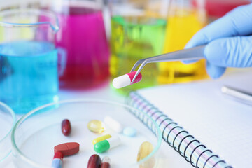 Scientist holds medical pill in forceps in laboratory closeup