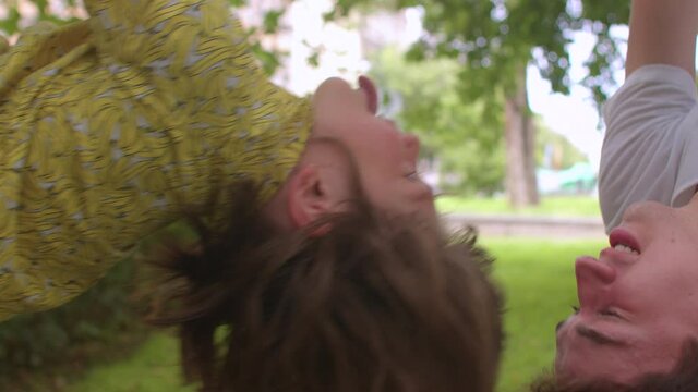 Boy showing tongue hanging upside down. Guys have fun in the city park. Babysitting as a part-time job for a pedagogical student during vacations.