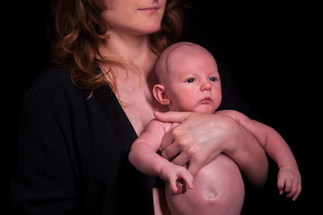 Happy woman mother holds a newborn baby boy in her arms, black studio background. Mom smiles with a child in her hands