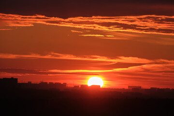 The big red sun sets at sunset behind the evening houses on the horizon