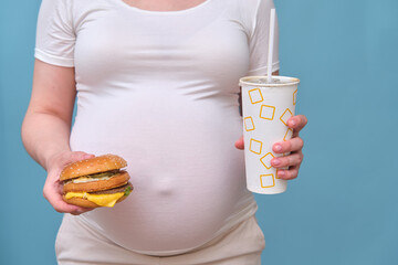 Pregnant woman with a burger and soda on a blue background, close-up