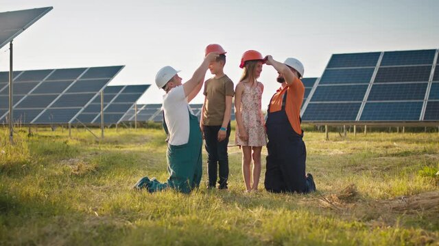 Two employees of the solar power plant brought their children to work and put a protective helmet on the children's heads. Children at work with the parents of power plant engineers. Father and child