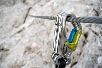 Via ferrata set with colorful carabiners hangs on a wire rope on a rocky mountain. - Powered by Adobe