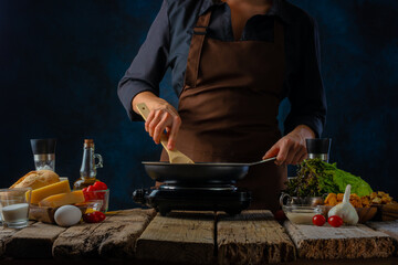 The chef prepares a classic Caesar salad. In a skillet, he mixes pieces of chicken fillet. Lots of salad ingredients. Wooden table. Restaurant, cafe, home cooking. Close-up.