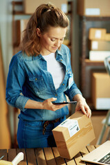 smiling female in jeans using phone applications in warehouse