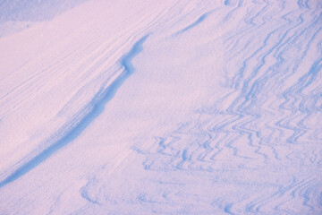 Beautiful winter background with snowy ground. Natural snow texture. Wind sculpted patterns on snow surface. Closeup top view with copy space.