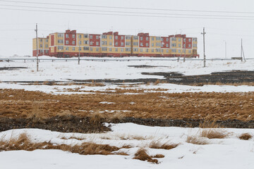 Fototapeta na wymiar View of the snowy tundra and colorful buildings during the snowfall. End of April. Cold spring in the Far North of Russia in the Arctic. Polar climate. Tavayvaam village, Chukotka, Siberia, Russia.
