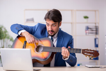 Young male employee playing guitar at workplace