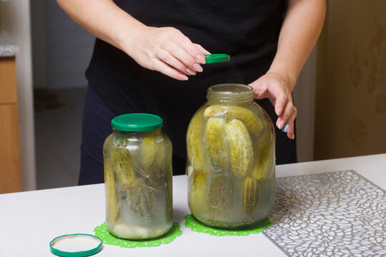 The woman closes the lid of a jar of cucumbers. Cucumbers are covered with pickling marinade. Harvest conservation.