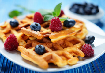 Homemade Belgian waffles served with fresh berries on white plate over wooden background