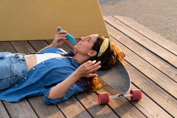 Trendy young girl lying on skateboard and recording voice message for smartphone application....