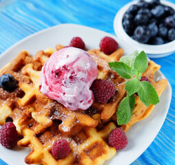Belgian waffles with fresh berries and ice cream over wooden background.