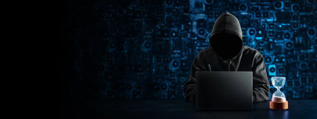 Hacker with a hidden face and with a laptop sits at the table, blue background. There is an...