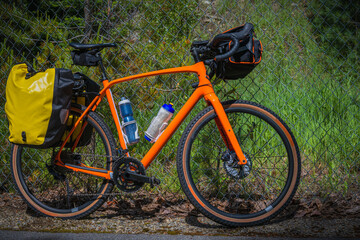 Naklejka premium 2021-06-14 ORANGE GRAVEL BIKE LOADED WITH BAGS LEANING AGAINST A CYCLONE FENCE