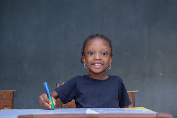 African girl child, pupil or student sitting down and writing in a classroom while studying for excellence in her education and career