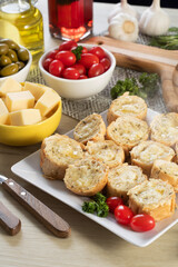 Garlic bread in white square plate on the table with cheese, rosemary, olives and cherry tomatoes.