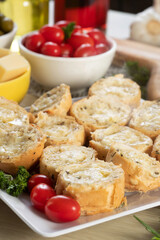 Garlic bread in white square plate on the table with cheese, rosemary, olives and cherry tomatoes.