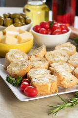 Garlic bread in white square plate on the table with cheese, rosemary, olives and cherry tomatoes.
