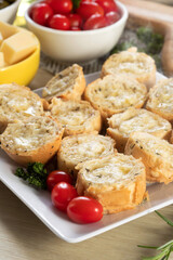 Garlic bread in white square plate on the table with cheese, rosemary, olives and cherry tomatoes.