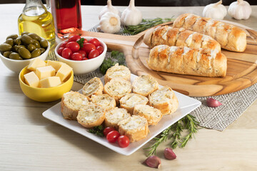 Garlic bread in white square plate on the table with cheese, rosemary, olives and cherry tomatoes.