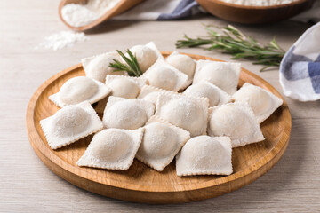 Uncooked ravioli and rosemary on white wooden table