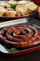 Sausage and garlic bread on a red plate on the barbecue table with appetizers, cheese, rosemary, olives and cherry tomatoes.