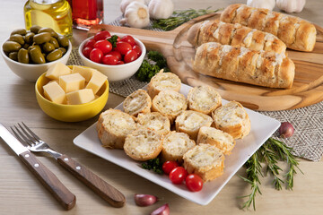 Garlic bread in white square plate on the table with cheese, rosemary, olives and cherry tomatoes. Top view.