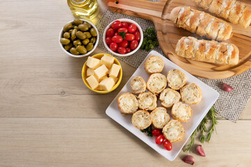 Garlic bread in white square plate on the table with cheese, rosemary, olives and cherry tomatoes. Top view.