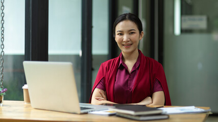 female smile and looks to camera, arms crossed, sitting in her working space