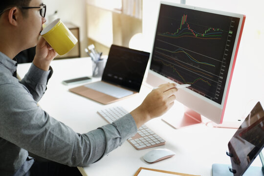 Investment professionals point their pen at their computer monitor to analyze the stock market for profit.