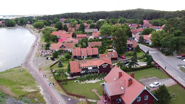 People pathway and red rooftops of Nida town in ascending drone view