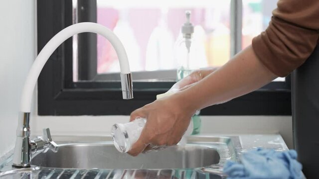 A man washes a glass of wine in the sink with soap and detergent