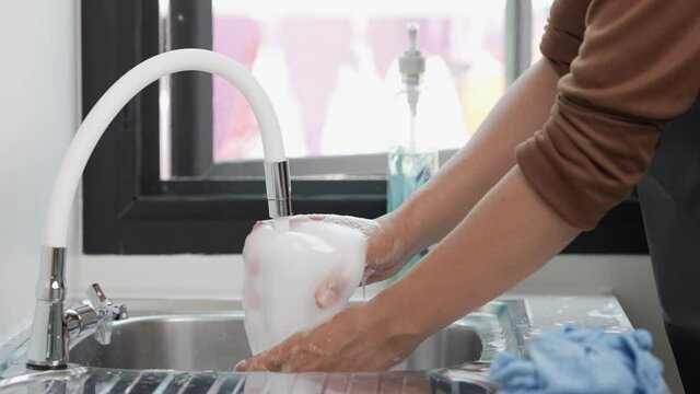 A man washes a glass of wine in the sink with soap and detergent