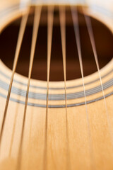 Fototapeta premium Detail of the body of a light wood guitar, the soundhole and strings.