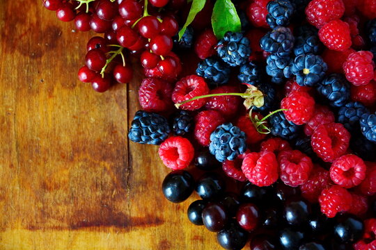 Black and red summer berries still-life. Mix berries bramble, blackberry, cherries, bunch red bird cherry and red raspberries on old wooden table. Top view with copy space