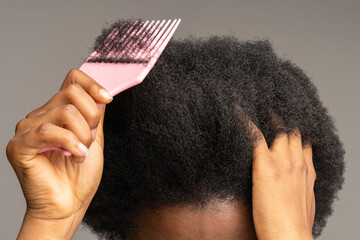 Close up of African American woman using pink plastic comb over studio gray wall background....