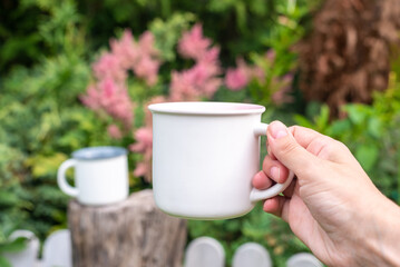 Mug mockup with bokeh green nature. Farmhouse rustic style. White mock up coffee cup in women hand. Blank mug printing design template.