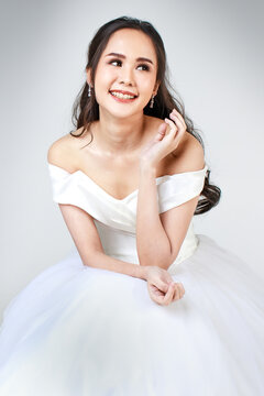 Young attractive Asian woman, soon to be bride, wearing white wedding gown sitting down looking happy. Concept for pre wedding photography