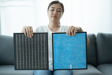 Beautiful Asian young woman holding a HEPA carbon air purifier filter in living room.