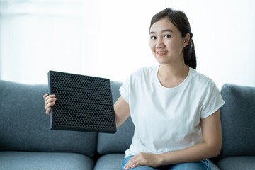 Beautiful Asian young woman holding a HEPA carbon air purifier filter in living room.