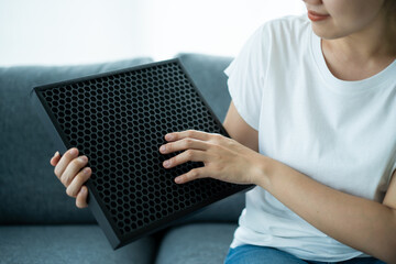Beautiful Asian young woman holding a HEPA carbon air purifier filter in living room.